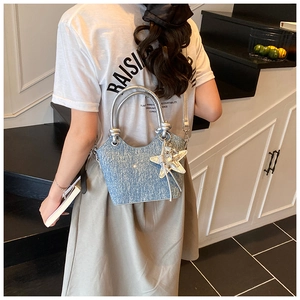 Detail of blue denim bucket bag featuring silver cylindrical handles and star charm accessory