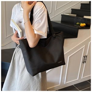 Detail of a large black tote bag featuring a minimalist leather brand logo and smooth texture
