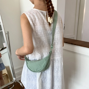 Lightweight pale green crescent crossbody bag styled on a model with white polka dot dress