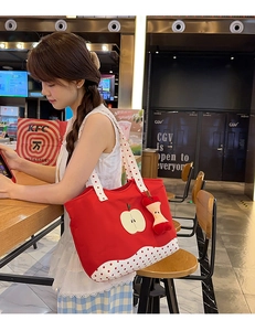 Detail of red canvas tote bag with polka dot straps and cute apple plush charm accessory