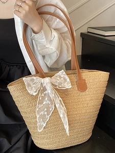 Large beige woven straw tote bag with white lace floral bow and brown leather straps