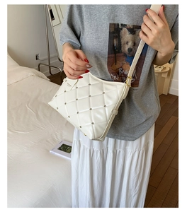 Close-up of beige quilted crossbody bag with gold rivet accents on a casual model