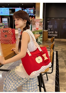 Detailed view of red canvas tote bag with apple print, polka dot strap, and plush charm
