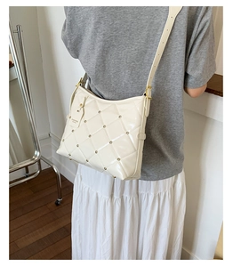 Detail view of quilted cream crossbody bag with gold studs and fashion tag on model
