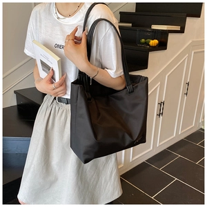 Close-up of minimalist black nylon tote bag with leather strap on a model's shoulder