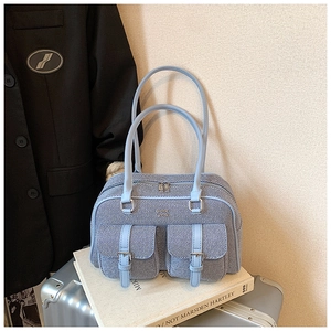 Detail of light blue denim Boston bag featuring flap pockets and silver metal buckles