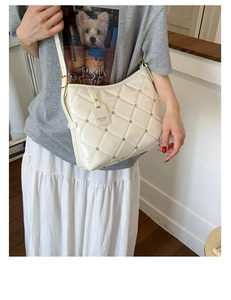 Close-up of cream quilted crossbody bag with metal rivets and adjustable shoulder strap