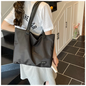 Rear view of a model wearing a large black nylon tote bag with MSDTON brand label