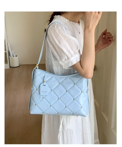 Detail of light blue quilted handbag with silver studs and fashion tag on white dress