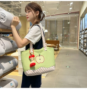 Detail of light green canvas tote bag with apple embroidery and red polka dot straps