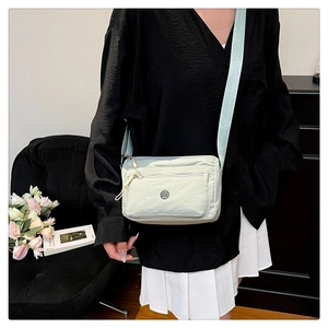 Close-up of light green nylon crossbody bag with multiple zippers and wide strap