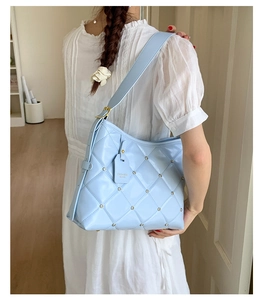 Detail of light blue quilted shoulder bag featuring small rhinestones and a gold buckle strap