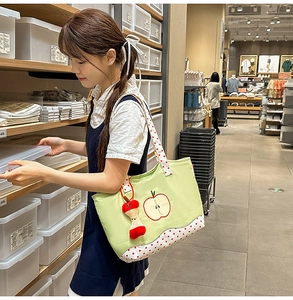 Detailed view of green canvas tote bag with apple embroidery and red polka dot strap