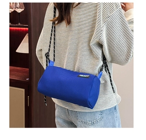 Detail view of a blue cylindrical canvas crossbody bag with a trendy rope shoulder strap