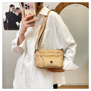 Detail view of khaki nylon crossbody bag with multiple zippers and adjustable wide strap