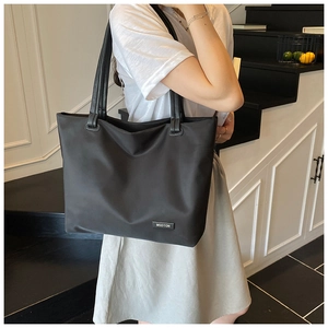 Model wearing a large black nylon tote bag with MSDTON logo in a modern indoor setting