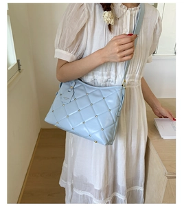 Close-up of light blue quilted leather shoulder bag with gold rivet accents and fashion tag