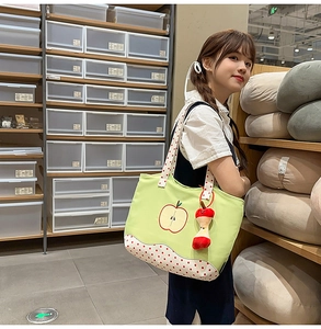 Detail of green apple print tote bag with polka dot straps and plush apple charm