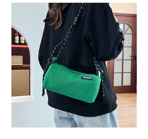 Close-up of green cylindrical canvas crossbody bag with decorative braided rope strap