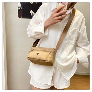 Khaki nylon crossbody bag with adjustable strap worn by a model in a casual indoor setting