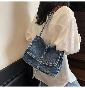 Detailed close-up of washed blue denim tote bag with brown leather strap and metal buckle