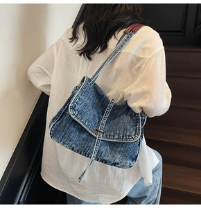 Detail of blue denim tote bag with metal buckle and red leather strap reinforcement