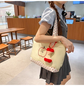 Detail of a beige tote bag with apple embroidery and red polka dot handles in a cafe
