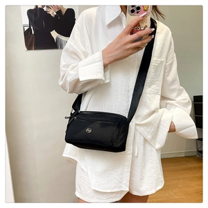 Practical black nylon crossbody bag worn by a model in a minimalist indoor setting