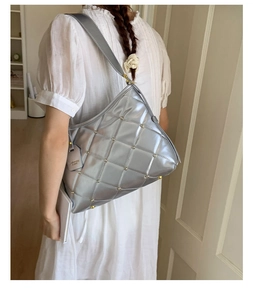 Close-up of silver quilted crossbody bag with gold rivets and wide strap on model