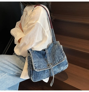 Detail of blue washed denim bag with red leather strap and silver buckle on stairs