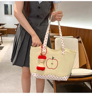 Detail of beige canvas tote with red apple embroidery and polka dot patterns