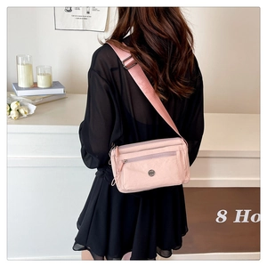 Detailed view of pink nylon crossbody bag with multiple functional zipper compartments