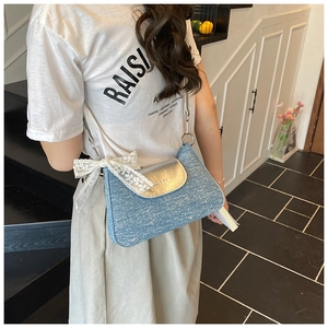 Detail of blue denim shoulder bag with silver metallic flap and white lace bow accessory