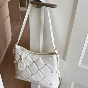Detail of white quilted leather texture with silver metal rivets on a luxury shoulder bag
