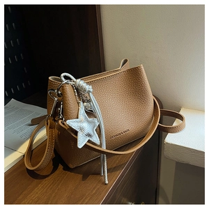 Détail du sac seau en cuir caramel avec pendentif étoile argenté sur fond en bois