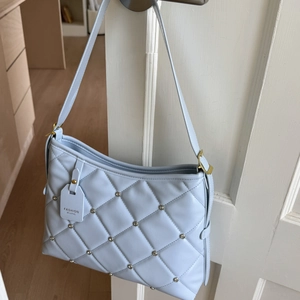 Detail of light blue quilted handbag with metal rivets and gold adjustable hardware
