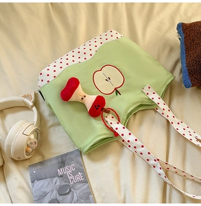 Detail of cute green polka dot apple tote bag with plush charm on beige bedding
