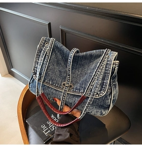 Detail of blue denim shoulder bag with dark red leather handle and metal buckle closure