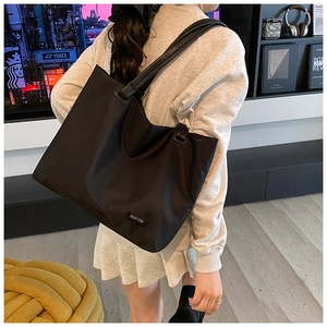 Detail view of black tote bag with leather straps and MSDTON brand plaque worn by model