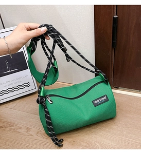 Close-up of green mesh cylinder crossbody bag with woven rope strap and brand label