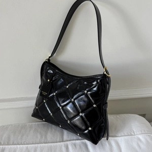 Détail d'un sac porté épaule noir matelassé avec clous argentés et bandoulière