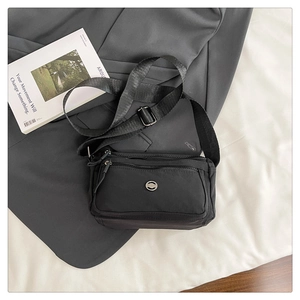 Detail view of black nylon crossbody bag with multi-layer zipper pockets and silver logo