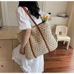 Detail of the woven hollow floral pattern and leather shoulder strap on the beige straw tote