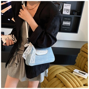 Detail of light blue crossbody bag with white lace trim and metal logo on smooth leather