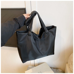 Detail of the large black satin nylon tote bag with leather handles and metallic logo