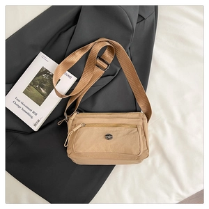 Detail of light brown nylon crossbody bag with multi-zipper layers and wide shoulder strap