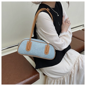 Detail view of a blue canvas baguette bag with brown leather trim and long shoulder straps