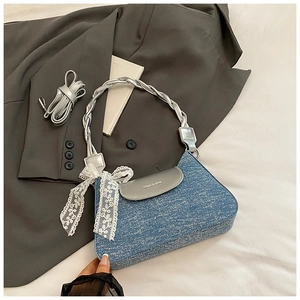 Detail of blue denim underarm bag featuring a silver flap and delicate white lace bow
