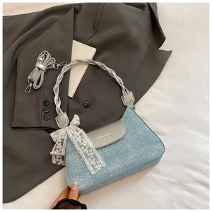 Detail of light blue denim handbag with silver flap, lace bow and braided handle