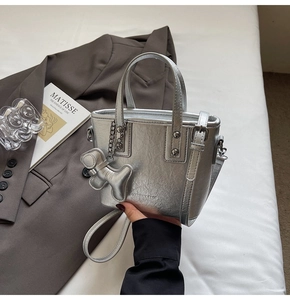 Detail of silver tote bag with metallic sheen, fashion text and cute dog charm pendant
